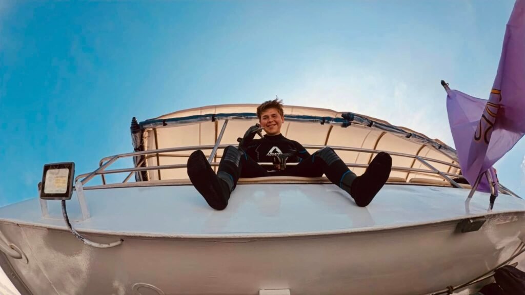 Person sitting on the edge of a boat smiling down at the camera with a blue sky in the background